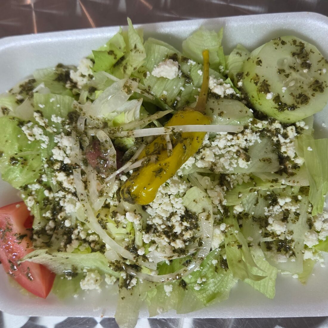 American Greek Salad — Combination of fresh iceberg lettuce, ripe tomatoes, cucumber, onion, crumbled feta, kalamata olives, pepperoncini peppers, and our house made vinaigrette